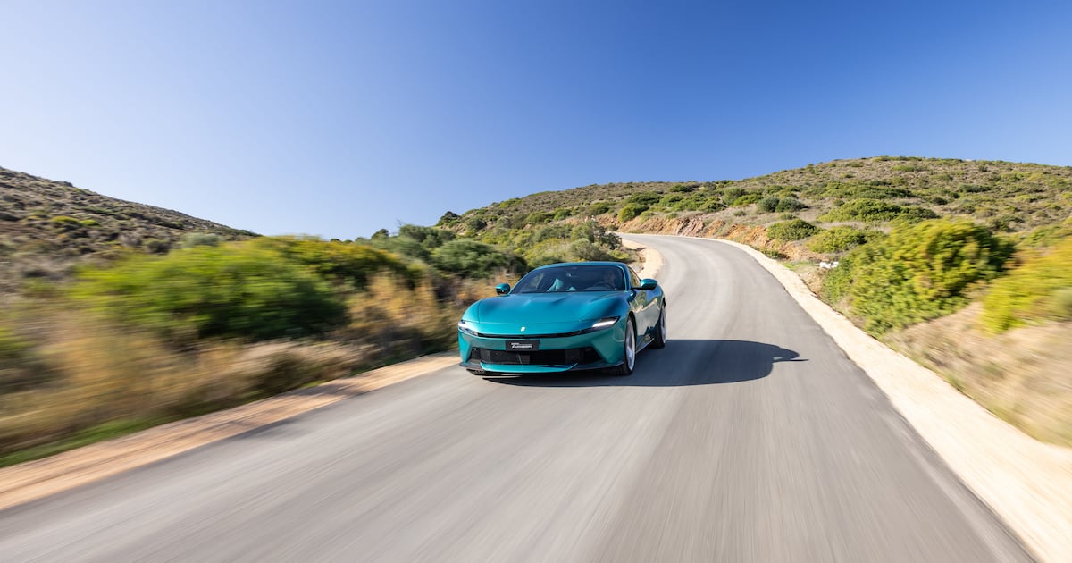 Ferrari Amalfi verde turquesa, vista frontal en movimiento sobre carretera sinuosa.