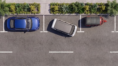 Vista aérea de estacionamiento con tres vehículos: sedán azul, Olinia Uno gris y blanco al centro, y otro vehículo compacto rojo, comparativa de tamaños de autos urbanos mexicanos