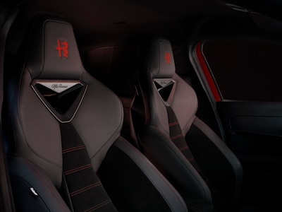 Detalle de asientos delanteros deportivos Sabelt del Alfa Romeo Junior 2026 tapizados en negro con costuras rojas y logo Alfa Romeo bordado en los reposacabezas interior de SUV híbrido mild hybrid 145 hp