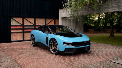 Ferrari Luce 2026 color azul cielo vista frontal tres cuartos estacionado frente a edificio, primer Ferrari completamente eléctrico de la historia con 1036 hp cuatro puertas y cinco asientos diseñado por Jony Ive y Marc Newson de LoveFrom
