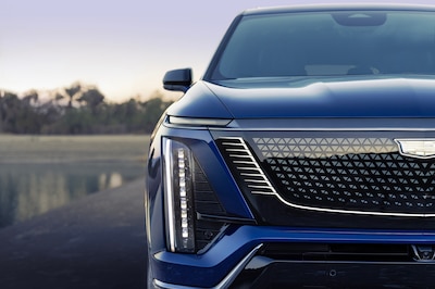 Detalle frontal del Cadillac Vistiq 2026 color azul oscuro mostrando parrilla cerrada con iluminación retroiluminada, faro LED vertical con proyectores individuales y emblema Cadillac horizontal, diseño eléctrico BEV3