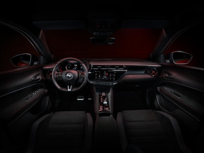 Interior Alfa Romeo Junior 2026 vista completa desde atrás con iluminación ambiental roja volante deportivo con logo Alfa Romeo cuadro de instrumentos digital Cannochiale pantalla central y consola con detalles en rojo SUV híbrido mild hybrid 145 hp