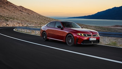 BMW M350 xDrive rojo, vista frontal tres cuartos en movimiento por carretera de montaña junto al mar
