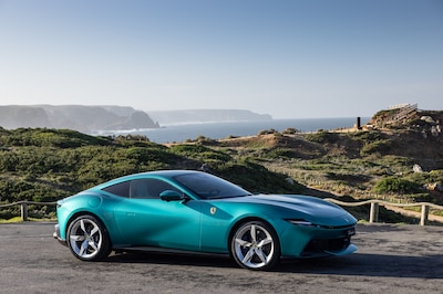 Ferrari Amalfi verde turquesa, vista lateral completa junto al mar con acantilados al fondo.