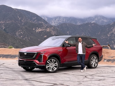 Carlos Sandoval posando frente al Cadillac Vistiq 2026 color rojo en carretera de montaña en California con nubes bajas al fondo, SUV eléctrico de tres filas con 615 hp y batería de 102 kWh