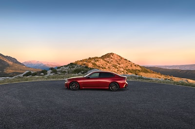 MW Serie 3 2027 rojo, vista lateral completa en carretera de montaña al atardecer
