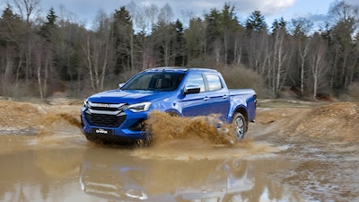 Isuzu D-MAX 2027 azul cruzando un lodazal con agua salpicando, bosque al fondo.