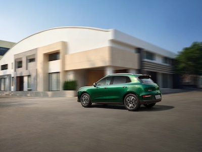 GWM ORA 5 2026 en verde, vista trasera tres cuartos en movimiento frente a edificio moderno