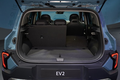 Cajuela abierta del Kia EV2 azul claro, con asiento trasero parcialmente abatido y placa EV2