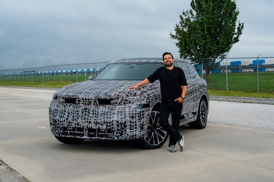 Carlos Sandoval junto al prototipo camuflado del nuevo BMW X5 2026 vista tres cuartos delantera en la planta de Spartanburg antes de su debut mundial