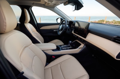 Interior Mazda CX-5 2025 vista desde puerta trasera mostrando asientos delanteros tapizados en piel beige consola central con palanca de cambios y pantalla táctil con vista al mar al fondo SUV compacto con nivel de refinamiento superior al segmento.