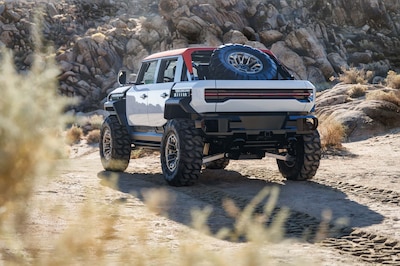 GMC HUMMER X concept pickup vista trasera tres cuartos en terreno rocoso desértico con llantas Goodyear off-road de gran tamaño rines beadlock llanta de refacción montada en la caja bicolor blanco y techo rojo concepto EV off-road de General Motors